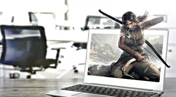 Lara Croft, postać z gry komputerowej, wychodzi z ekranu laptopa, gotowa do akcji z łukiem i czekana.