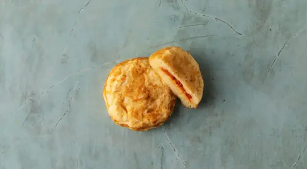 Två gyllene plättar, en hel och en delad, med en röd fyllning. Perfekta pannkakor för frukost eller fika.