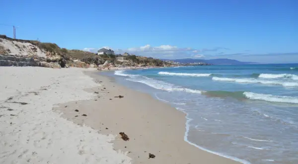 Arena dorada y aguas turquesas en la playa Remior, con algunas personas disfrutando del sol y el mar.