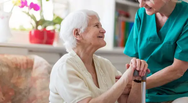 Une aide-soignante soutient une résidente souriante. Une maison de retraite moins cher offre un cadre de vie agréable et sécurisé.