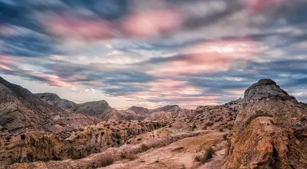 Paisaje desértico con formaciones rocosas y un cielo dramático al atardecer, evocando la belleza del volcan Almería.