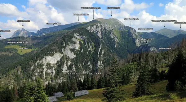 Widok na Tatry z Doliną Kościeliską. W oddali szczyty: Giewont, Ciemniak, Tomanowy Wierch Polski. Na pierwszym planie widać drewniane hale stoły.