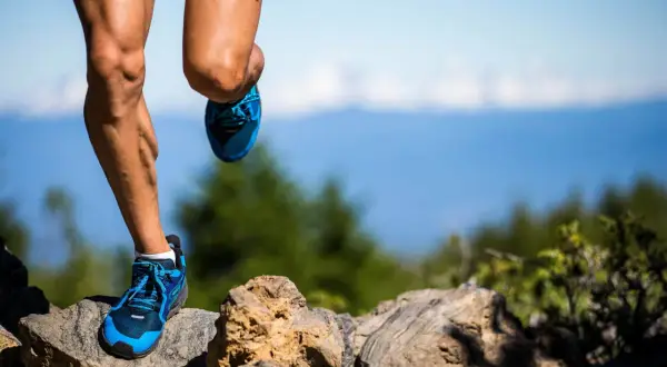 Nogi biegacza w niebieskich butach na kamienistym szlaku, przygotowującego się do ultramaratonu. Ile km? Tego nie wiemy, ale wysiłek jest widoczny.