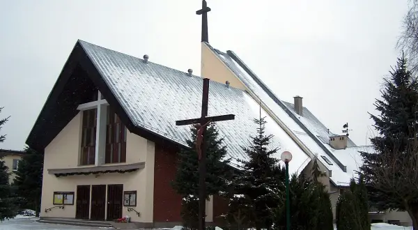 Kościół w Robakowie zimą, pokryty śniegiem, z krzyżem przed fasadą.