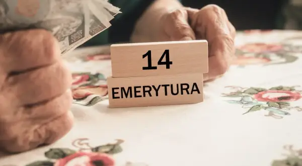 Dłonie seniora trzymają pieniądze. Na drewnianych klockach napis "14 EMERYTURA". Czekamy na 14 emeryturę 2025 netto.