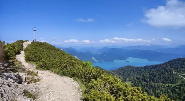 Gipfelkreuz nach einer Heimgarten Wanderung mit Blick auf einen türkisfarbenen See und Berge.
