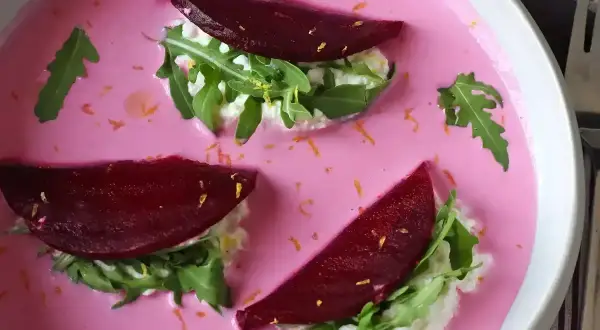 Vacker vegetarisk mat: rödbetor, ruccola och färskost i en rosa soppa, garnerad med rivet citronskal.