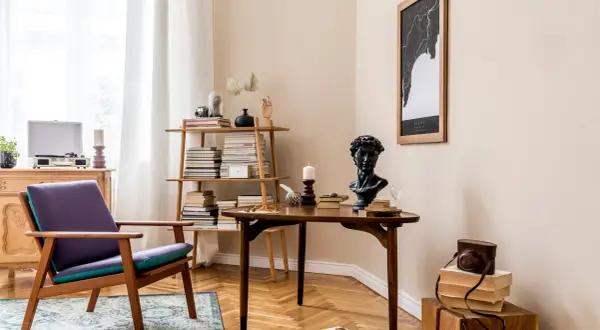Stylowe wnętrza retro: fioletowy fotel, drewniany stolik z popiersiem i książkami, regał pełen literatury, gramofon i mapa na ścianie.