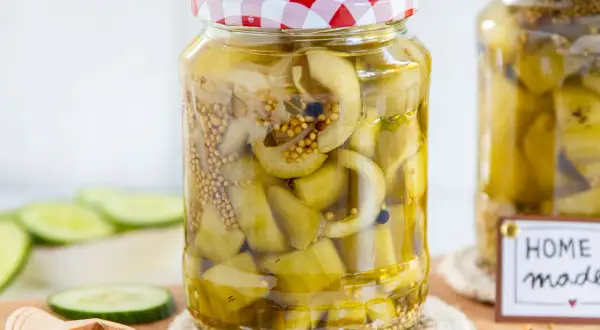 Glas mit eingelegten Senfgurken, perfekt für ein Senfgurken Rezept. Frische Gurkenscheiben und Senfkörner sind sichtbar.