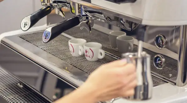 Mano che prepara un caffè con la bar macchina caffè. Due tazzine bianche attendono il loro turno.