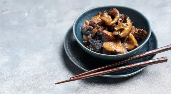 Deliciosas setas shiitake salteadas en un cuenco azul, listas para ser disfrutadas con palillos.