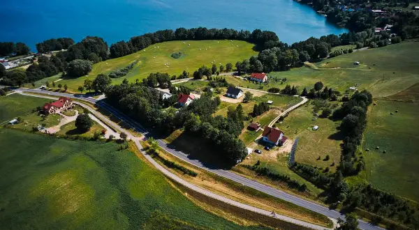 Malownicze **trasy rowerowe Mazury** wiodą przez zielone pola i lasy, w pobliżu błękitnego jeziora.