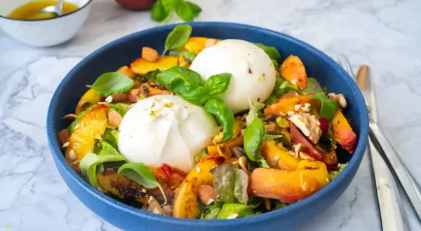 Pfirsich-Burrata-Salat mit Nüssen und Basilikum in blauer Schüssel.