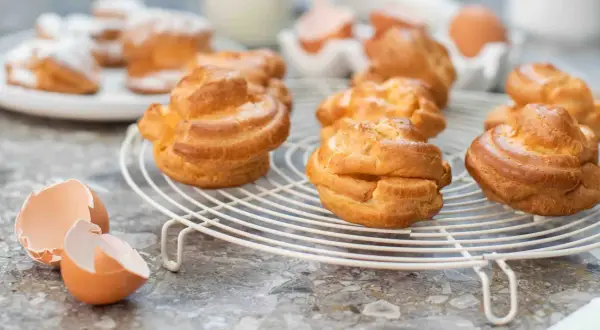 Färska petit choux på ett galler, med äggskal i förgrunden. Perfekt för en fika!