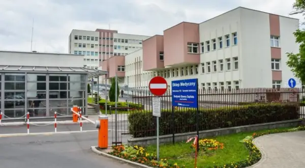 Nowoczesny budynek szpitala z bramkami wjazdowymi i znakami informacyjnymi.