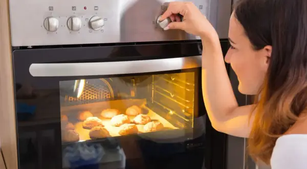 Kobieta ustawia temperaturę piekarnika, zastanawiając się, ile prądu zużywa piekarnik podczas pieczenia ciasteczek.
