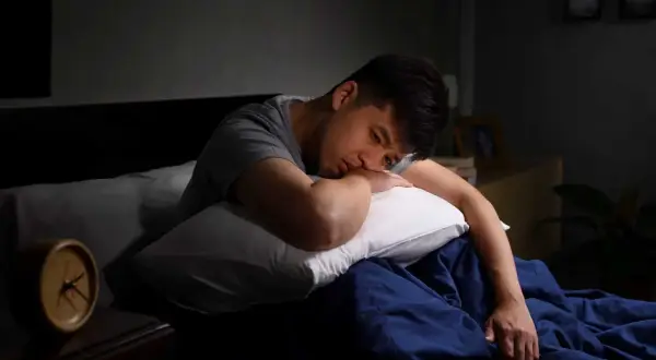 En man ligger i sängen, ser ut att kämpa med depression eller utmattning. Klockan på nattduksbordet visar att natten är lång.