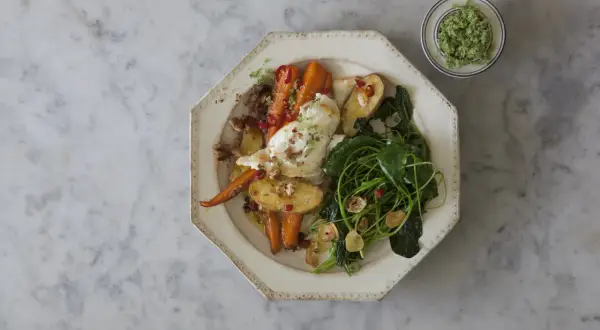 Ugnsrostade rotfrukter med fetaost, serverade med gröna blad och en grön topping.