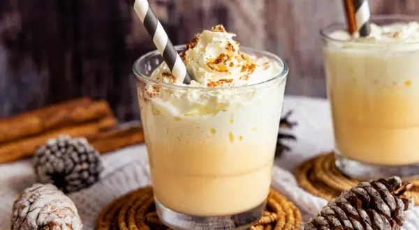 Zwei Gläser Bombardino mit Sahne und Zimt, dekoriert mit Tannenzapfen und Zimtstangen.