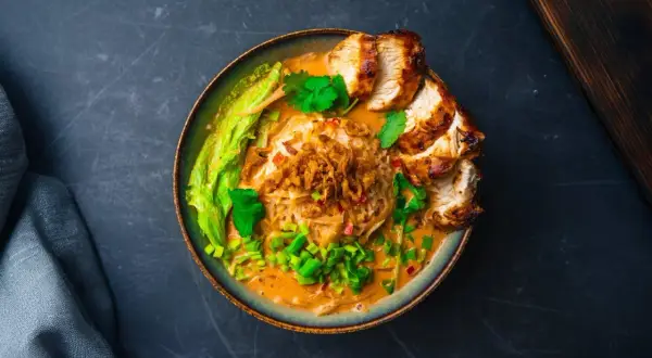Aksamitny, kremowy tan tan ramen z kawałkami grillowanego kurczaka, chrupiącą cebulką i świeżą kolendrą.