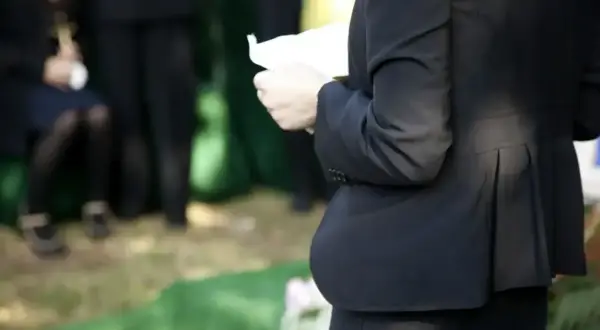 Smutne wspomnienie o zmarłej osobie. Kobieta w czerni trzyma kartkę, być może przemówienie pożegnalne.