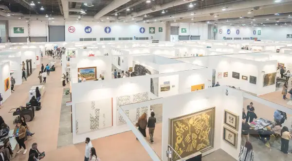 A bustling scene at the Mexico City Art Fair, with visitors exploring numerous white-walled booths showcasing diverse artworks.