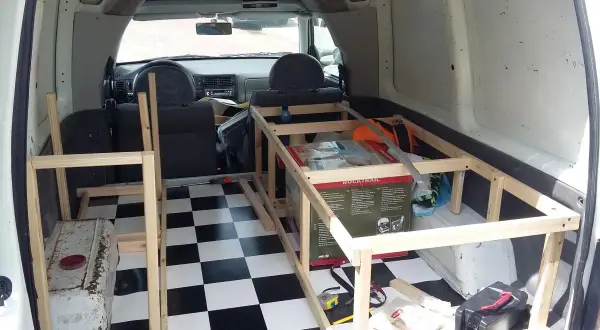 Wnętrze vana przerabiane na minicamper. Drewniana konstrukcja łóżka, szachownica na podłodze, skrzynka narzędziowa.