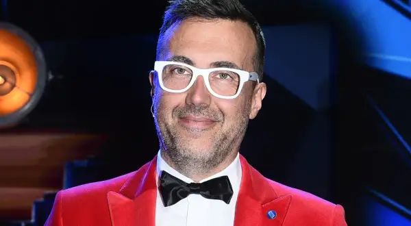 DJ Adamus w czerwonej marynarce i białych okularach, z czarną muszką.