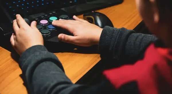 Dłonie gracza na joysticku i klawiaturze, obok myszka komputerowa.