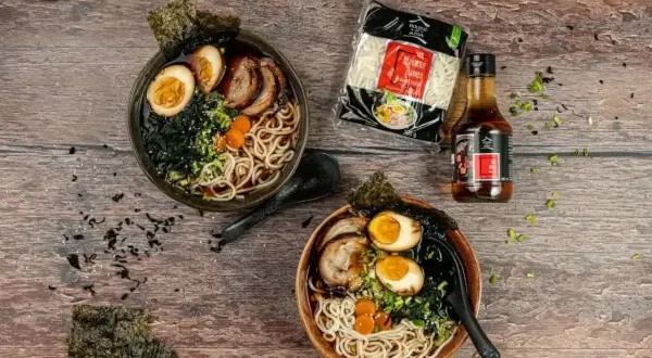 Dwie miski domowego ramenu z jajkiem, mięsem i nori, obok makaron i sos.