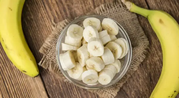 Dwa banany, jeden w całości, drugi pokrojony w plasterki w szklanej miseczce. Zastanawiasz się, ile węglowodanów ma banan?