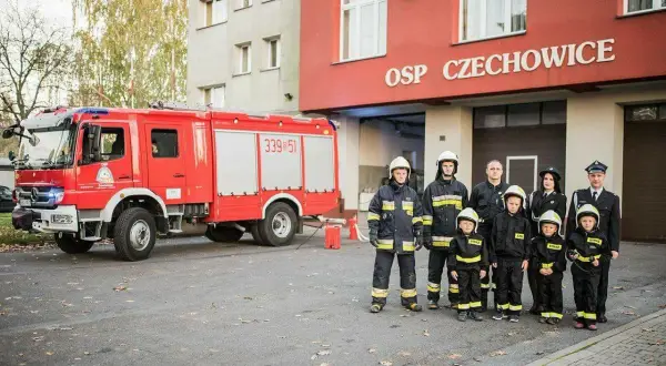 Strażacy OSP Czechowice z wozem strażackim i dziećmi w strojach strażackich.