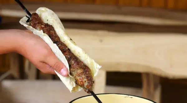 Ręka trzyma lula kebab zawinięty w placek. Mięso jest soczyste i rumiane, gotowe do jedzenia.