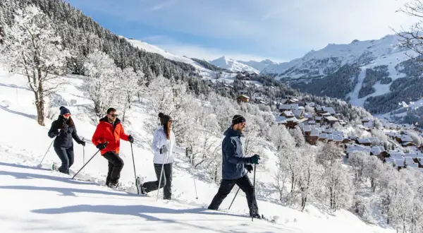 Quatre personnes font une randonnée en raquettes à Méribel en hiver, profitant du paysage enneigé et des montagnes.