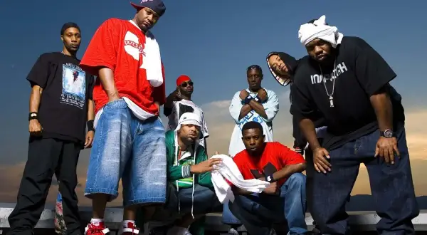 Grupa raperów z Wu-Tang Clan pozuje do zdjęcia na tle nieba.