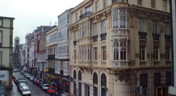 Edificios con balcones acristalados y una torre ornamental en una calle de Ferrol. Merece la pena visitar Ferrol por su arquitectura única.