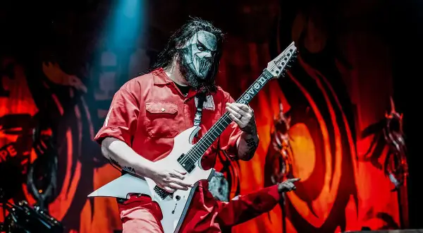 Muzyk Slipknot w czerwonym kombinezonie i masce gra na białej gitarze. Zapowiedź nowego albumu Slipknot.