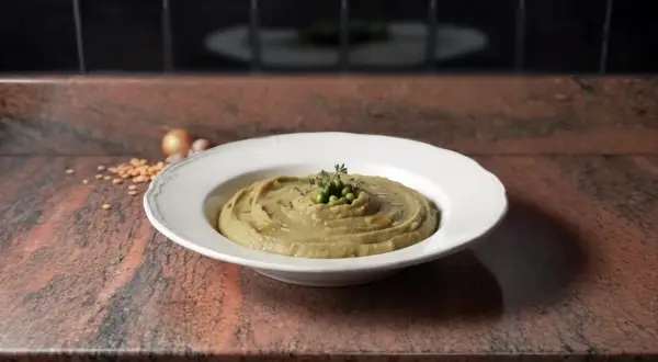 Une assiette de purée de pois cassés, garnie de petits pois et d'herbes, sur un plan de travail en granit.