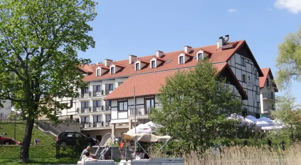 Hotel Anek Mrągowo nad jeziorem, z łodzią przy pomoście i zielenią.