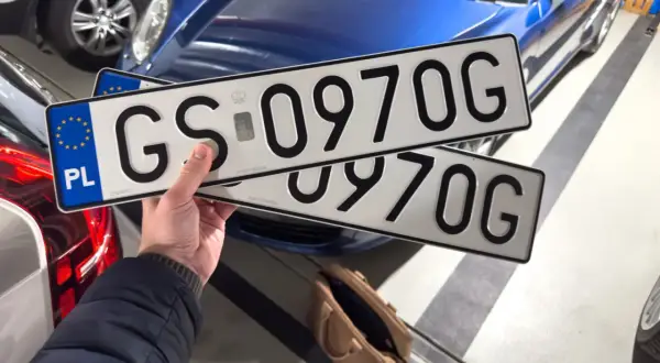 Ręka trzyma tablice rejestracyjne GS 0970G, gotowe do rejestracji samochodu online.