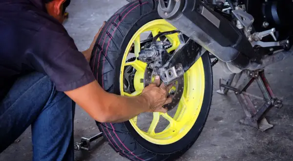 Mechanik wymieniający oponę w motocyklu z żółtą felgą.