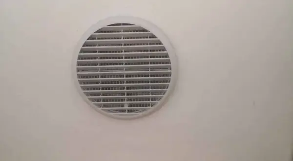 Foro ventilazione cucina entra freddo. La griglia bianca circolare è montata su una parete chiara.