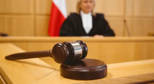 Młotek sędziowski na stole w sali sądowej, obok polska flaga. Sędzia w todze w tle. Ile apelacji jest oddalanych?