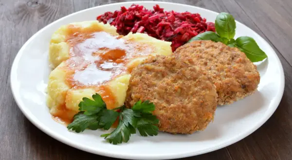 Dwa złociste mielone z piekarnika, podane z purée ziemniaczanym polanym sosem, surówką z buraków i listkami bazylii.