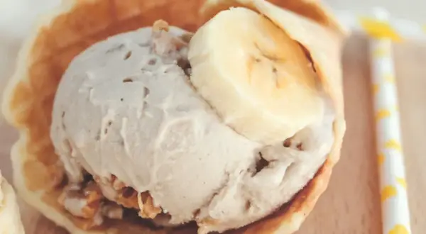 Delicioso helado de crema de cacahuete en un cono de gofre, coronado con rodajas de plátano.