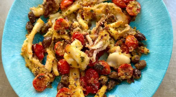 Deliziosi calamari gratinati al forno, croccanti e saporiti, con pomodorini e olive, serviti su un piatto blu.