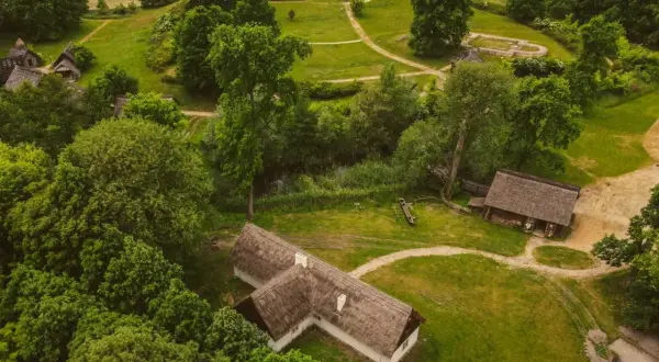 Rezerwat archeologiczny Zawodzie, z widokiem na drewniane chaty i zalesione wzgórza, ukazuje dawne osadnictwo.