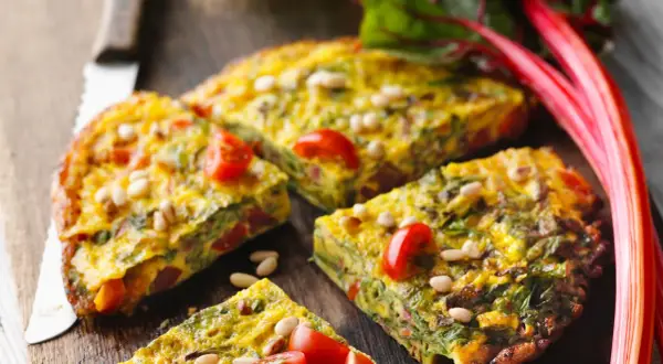 Tortilla de acelgas con tomates cherry y piñones, cortada en porciones sobre una tabla de madera.