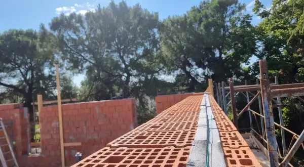 Costruzione di una muratura portante in laterizio, con mattoni forati rossi e blocchi in cemento.