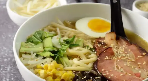 Jak zrobić ramen? Miska pełna aromatycznego bulionu z makaronem, plastrem boczku, jajkiem na pół, pak choi, kukurydzą i grzybami mun.